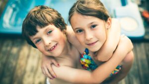 kids in swimsuits embrace looking at camera